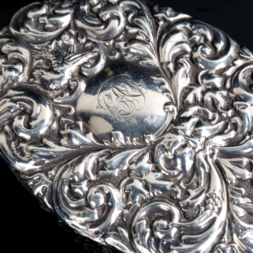 494 - A heavy late Victorian silver dressing table hand mirror, allover relief embossed foliate decoration... 