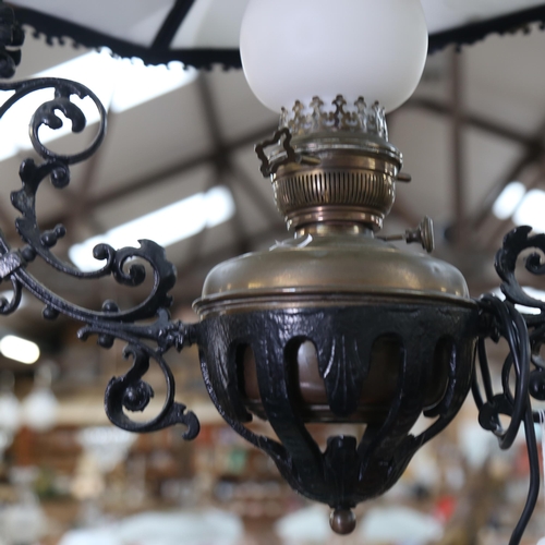 293 - A wrought-iron framed brass ceiling oil lamp, with milk glass panels and milk glass chimney, overall... 