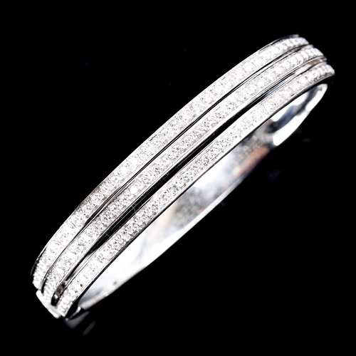 63 - A modern 18ct white gold diamond hinged bangle, triple-row openwork settings with modern round brill... 