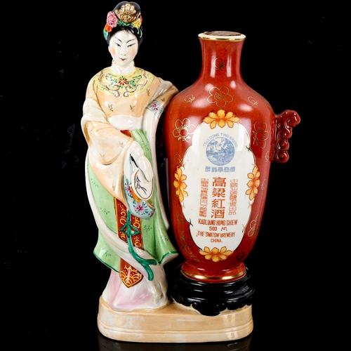 1090 - A bottle of Chinese Kaoliang Hung Chiew wine in sealed porcelain bottle, flanked by a figure of a wo... 