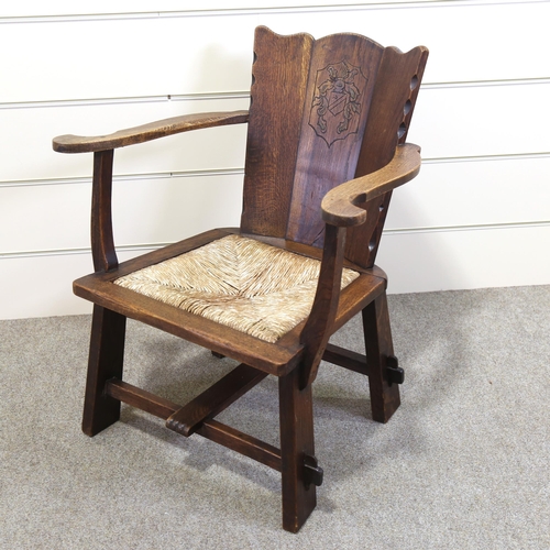 1152 - An oak-framed elbow chair, with carved armorial crest and rush seat, seat width 52cm