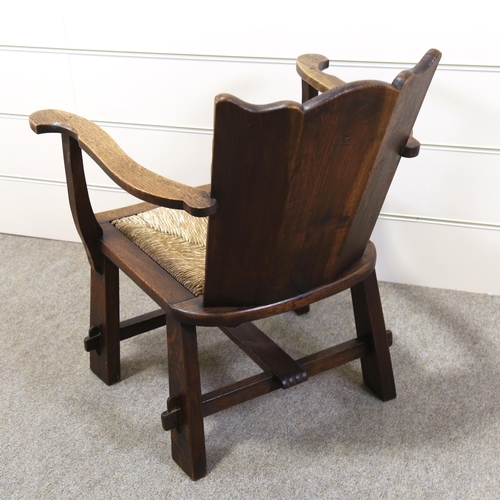 1152 - An oak-framed elbow chair, with carved armorial crest and rush seat, seat width 52cm