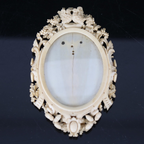 167 - A 19th century carved and pierced ivory oval photo frame, bird grapevine and acorn decoration, with ... 