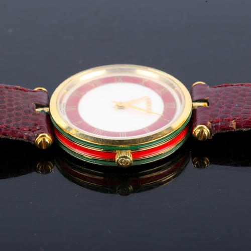 32 - GUCCI - a mid-size gold plated quartz wristwatch, white and red dial with gilt Roman numeral hour ma... 