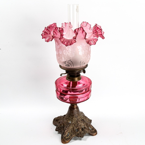 1054 - A Victorian oil lamp with faceted cranberry glass font, on cast-iron base, frilled cranberry shade, ... 