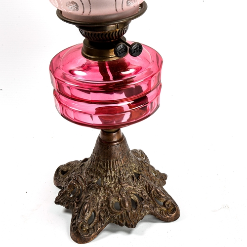 1054 - A Victorian oil lamp with faceted cranberry glass font, on cast-iron base, frilled cranberry shade, ... 