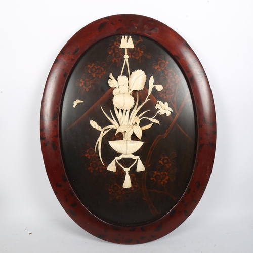 259 - A Japanese oval lacquer panel, circa 1900, with applied carved bone decoration, in red lacquer frame... 