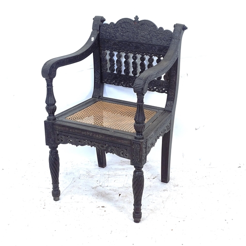 2250 - An ornate ebonised Victorian armchair, with allover relief carved decoration and cane panel seat