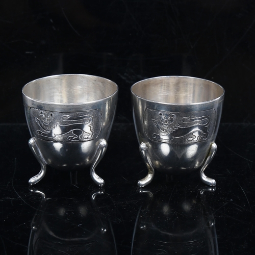 1126 - A pair of Continental silver egg cups, with engraved lion decoration on 3 feet, stamped 800