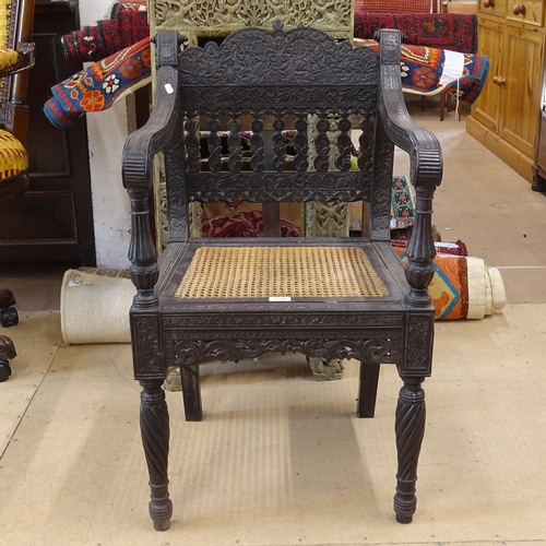 2250 - An ornate ebonised Victorian armchair, with allover relief carved decoration and cane panel seat