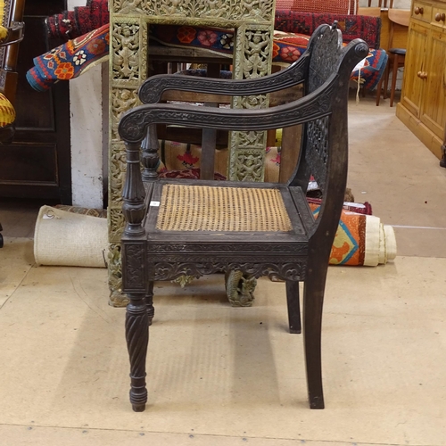 2250 - An ornate ebonised Victorian armchair, with allover relief carved decoration and cane panel seat