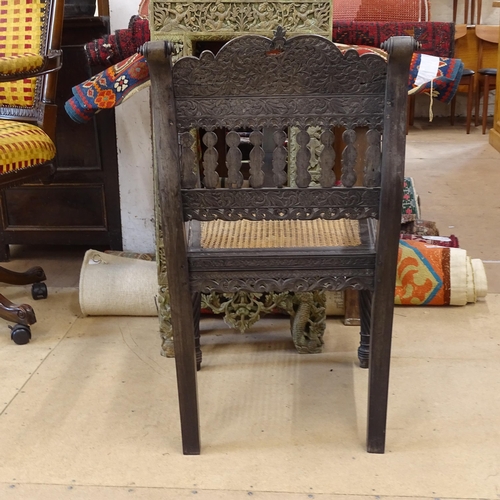 2250 - An ornate ebonised Victorian armchair, with allover relief carved decoration and cane panel seat