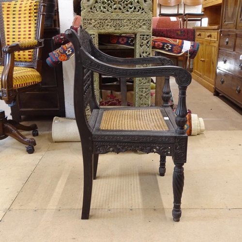 2250 - An ornate ebonised Victorian armchair, with allover relief carved decoration and cane panel seat