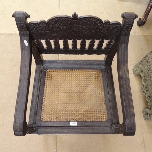 2250 - An ornate ebonised Victorian armchair, with allover relief carved decoration and cane panel seat