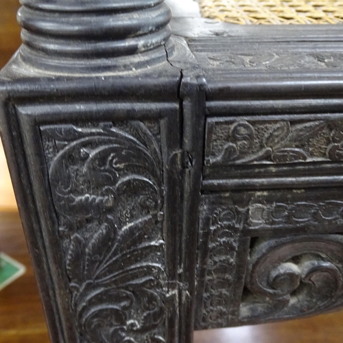 2250 - An ornate ebonised Victorian armchair, with allover relief carved decoration and cane panel seat