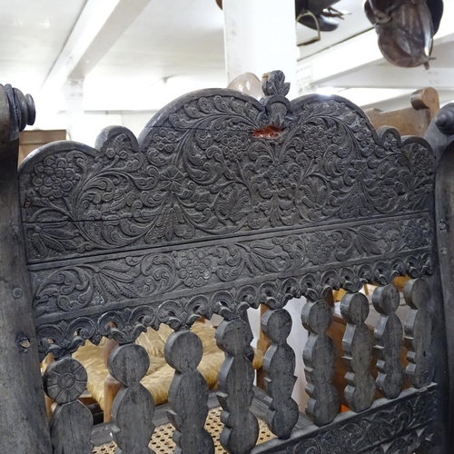 2250 - An ornate ebonised Victorian armchair, with allover relief carved decoration and cane panel seat