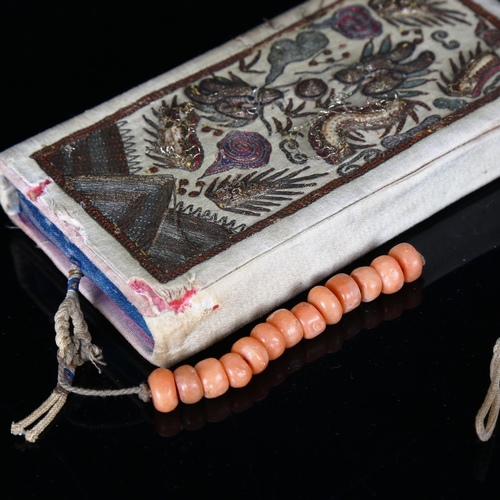 1135 - A Chinese embroidered silk case, containing a blue silk covered notebook and a short string of coral... 