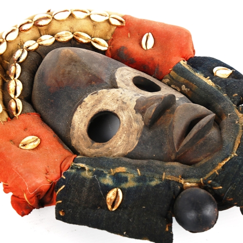 1357 - An African Dan carved and painted wood mask, with cowrie shell and textile surround, length 32cm