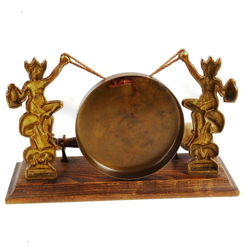 1118 - A brass gong supported by imp figures, on oak base, length 28cm