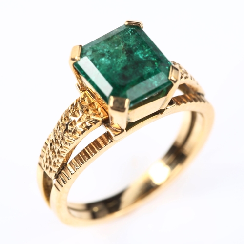 110 - A late 20th century solitaire emerald ring, unmarked gold settings with textured shoulders and squar... 