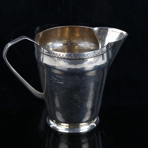 313 - An Arts and Crafts style silver cream jug, plain tapered cylindrical form, with hand engraved rim an... 