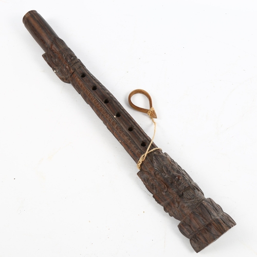 1074 - An Oriental carved hardwood flute with mask designs, length 35cm