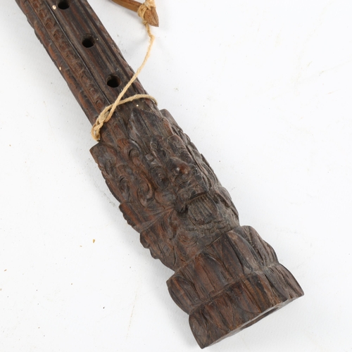 1074 - An Oriental carved hardwood flute with mask designs, length 35cm