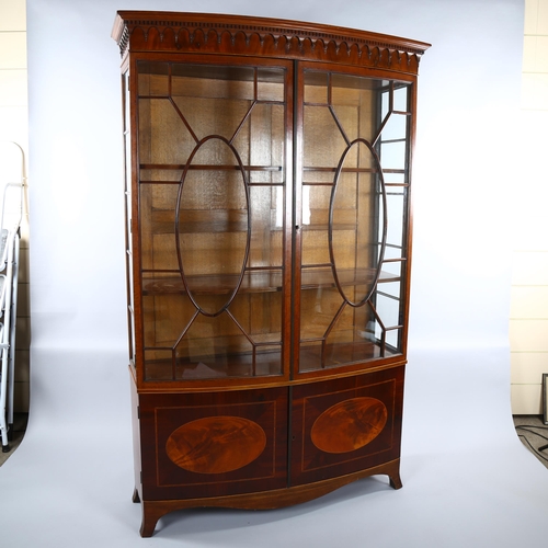 1235 - An Edwardian inlaid mahogany bow-front display cabinet in Sheritan style, with carved cornice and cu... 