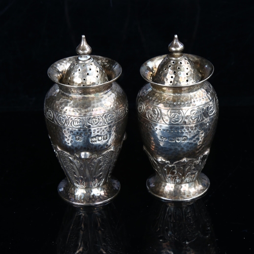 423 - A pair of Arts and Crafts Edwardian silver pepperettes, planished and relief embossed acanthus leaf ... 