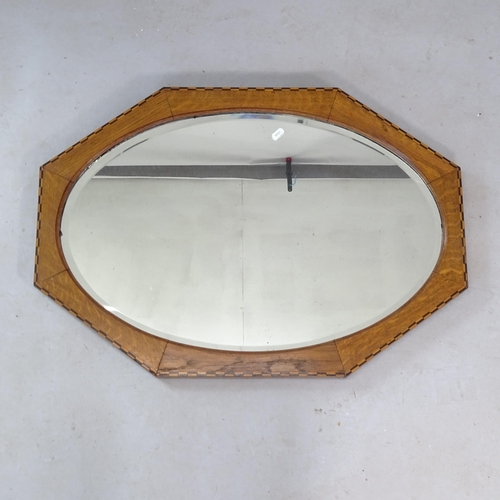 2329 - An oak 1930s oval bevel-edge wall mirror, in octagonal frame with inlaid decoration, 84cm x 58cm