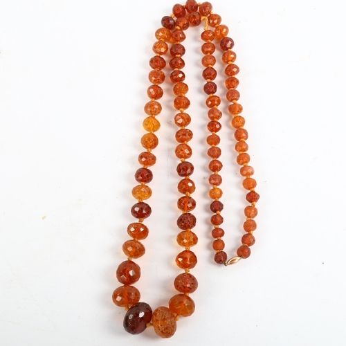 209 - A long graduated faceted amber bead necklace, with unmarked rose gold barrel clasp, beads ranging fr... 