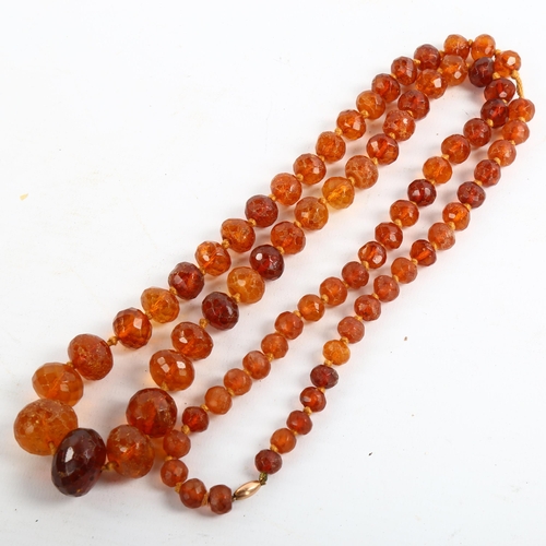 209 - A long graduated faceted amber bead necklace, with unmarked rose gold barrel clasp, beads ranging fr... 