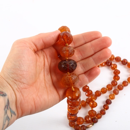 209 - A long graduated faceted amber bead necklace, with unmarked rose gold barrel clasp, beads ranging fr... 