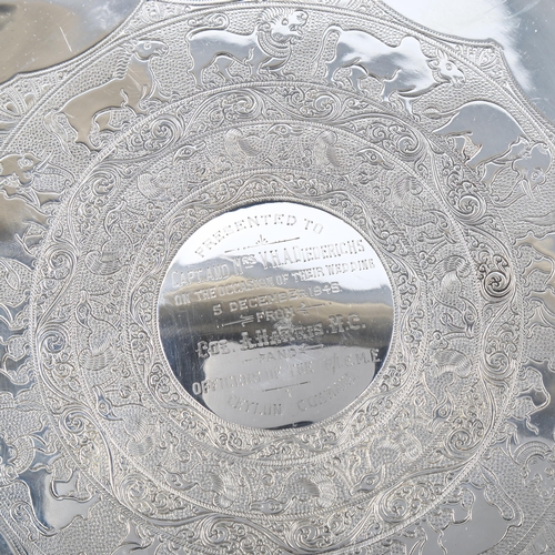 544 - A George V silver salver, circular form with scalloped rim and Indian inspired engraved animal decor... 