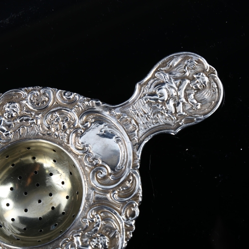 578 - A large German silver tea strainer, with relief embossed cherub and foliate decoration, length 14.5c... 