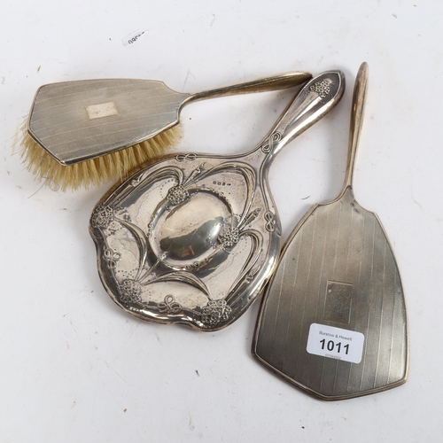 1011 - An engine turned silver-backed dressing table mirror and matching brush, and an Art Nouveau silver-b... 