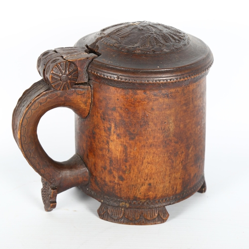 1001 - An 18th century Scandinavian birch peg tankard, with carved hinged lid, resting on 3 carved feet, he... 