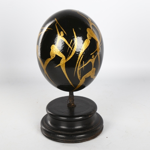 1148 - Manner of Matisse, hand painted ostrich egg, decorated with gilded hunting figures, on ebonised wood... 