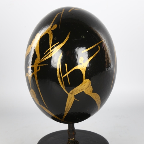 1148 - Manner of Matisse, hand painted ostrich egg, decorated with gilded hunting figures, on ebonised wood... 