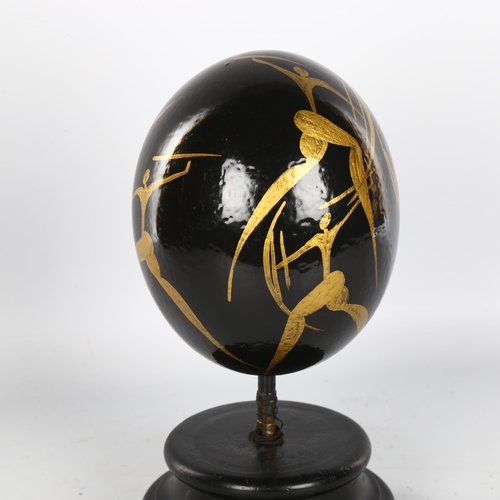 1148 - Manner of Matisse, hand painted ostrich egg, decorated with gilded hunting figures, on ebonised wood... 