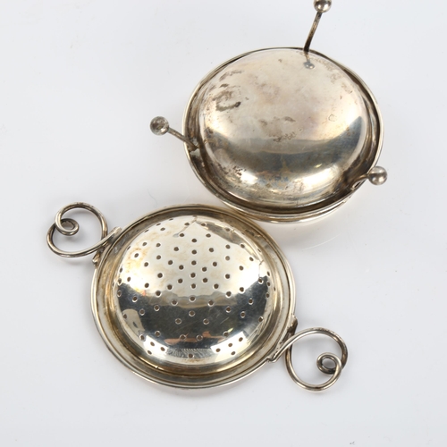 611 - An Arts and Crafts George V silver 2-handled tea strainer and stand, with wire heart-shaped handles,... 