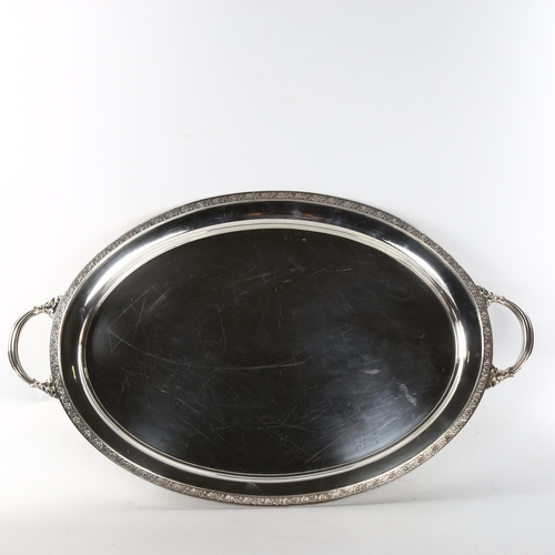 622 - A large and heavy silver 2-handled tea tray, oval form with relief floral rim raised on 4 foliate fe... 