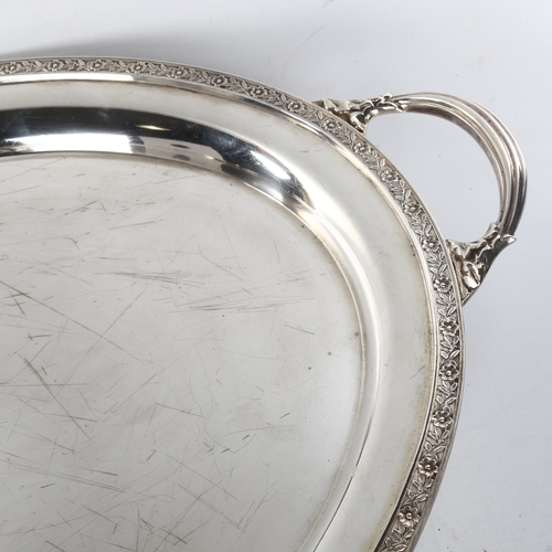 622 - A large and heavy silver 2-handled tea tray, oval form with relief floral rim raised on 4 foliate fe... 