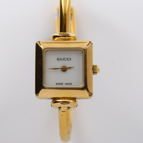 64 - GUCCI - a lady's gold plated 1900L quartz bracelet watch, square white dial with bangle bracelet, se... 