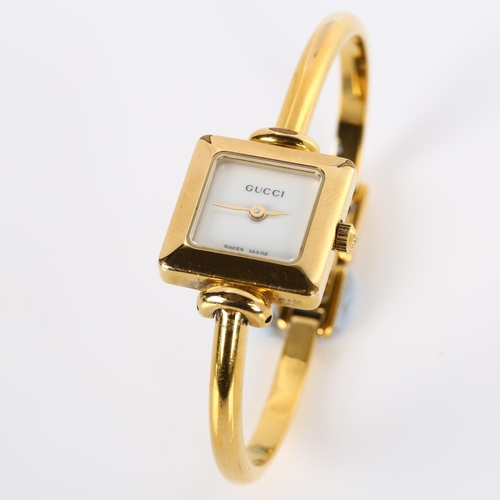 64 - GUCCI - a lady's gold plated 1900L quartz bracelet watch, square white dial with bangle bracelet, se... 