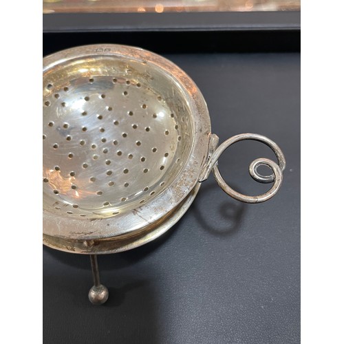 611 - An Arts and Crafts George V silver 2-handled tea strainer and stand, with wire heart-shaped handles,... 