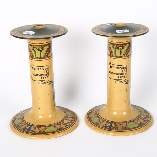 349 - A pair of stoneware candlesticks, with figures and motto decoration, height 21cm