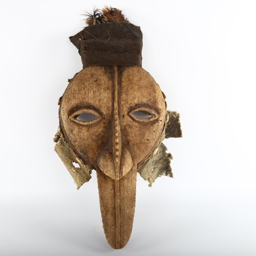 1062 - An African carved wood Tribal mask, with textile and shell surround and feather plumage, height 52cm