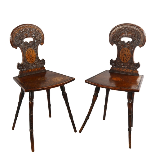 1079 - A pair of 19th century Swiss hall chairs, with ornate relief carved backs and inlaid panels, part of... 