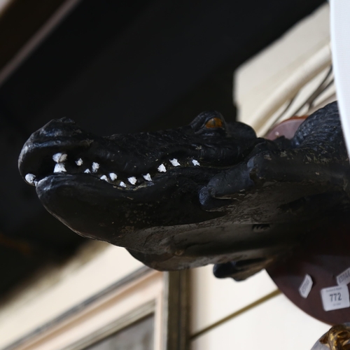 772 - A painted and moulded study of an alligator's head with glass eyes, mounted on shield plinth